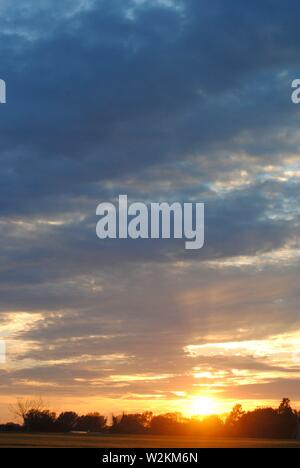 Sonnenuntergang über die Felder von Suffolk, Sommer orange-gelbe Sonne mit dunklen Wolken Stockfoto