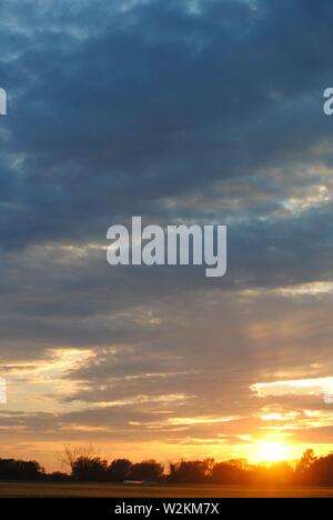 Sonnenuntergang über die Felder von Suffolk, Sommer orange-gelbe Sonne mit dunklen Wolken Stockfoto