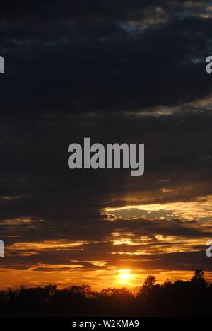 Sonnenuntergang über die Felder von Suffolk, Sommer orange-gelbe Sonne mit dunklen Wolken Stockfoto