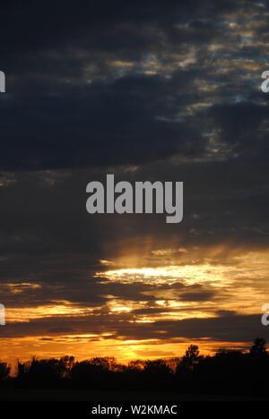 Sonnenuntergang über die Felder von Suffolk, Sommer orange-gelbe Sonne mit dunklen Wolken Stockfoto