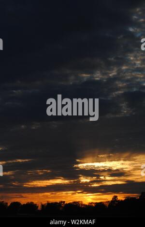 Sonnenuntergang über die Felder von Suffolk, Sommer orange-gelbe Sonne mit dunklen Wolken Stockfoto