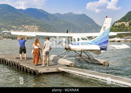 Comer see, Comer See, Italien - JUNI 2019: Junges Paar wartet auf eine Cessna 206 Stationair Wasserflugzeug betrieben von der Aero Club Como am Comer See. Stockfoto