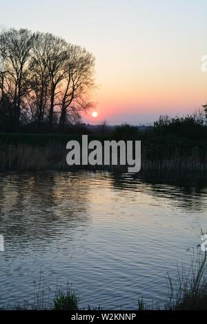 Bilderserie eines Sonnenuntergangs über einem englischen Fluss mit Silhouettenplänen und Bäumen im Herbst. Stockfoto