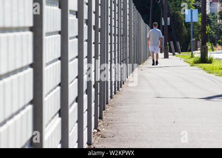 Ältere Menschen laufen auf Asphalt neben Beton Zaun auf der Straße Stockfoto