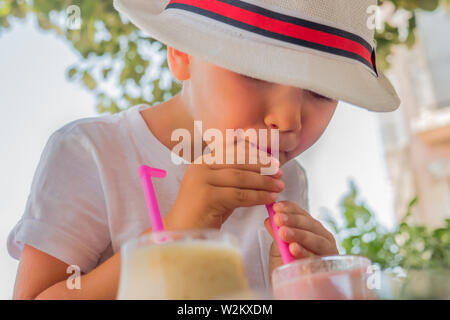 Getränke für Kinder, Kinder. Junge in den Hut trinken Cocktail im Freien. Cafe, freundlich zu Kindern. Glückliche Kindheit Konzept. Sommer erfrischenden Drink mit Stockfoto