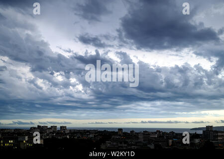 Dunklen stürmischen Himmel über einer Stadt am Meer im Sommer Abend. Dramatische Skyscape mit großen, grauen Wolken. Verschiedenen Wolkentypen und atmosphärische Phänomene. Stockfoto
