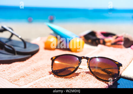Sommer Urlaub: Handtuch mit anderen Strand Zubehör wie eine Sonnenbrille, Sonnencreme und Flip Flops am Meer Stockfoto