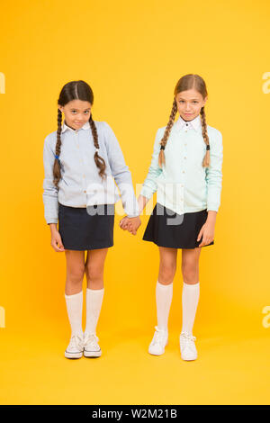 Gefühl schüchtern. Süße Kinder, Hände auf gelben Hintergrund. Kleine Kinder tragen Schuluniform. Schule Kinder mit Mode schauen. Kleine Kinder mit geflochtenem Haar sind zurück in die Schule. Stockfoto