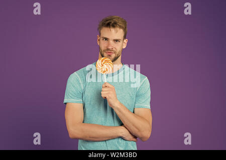 Geschmack der Kindheit. Mann schöner macho Essen großen bunten süßen Lutscher. Mann mit Borsten mag Lollipop. Cheat meal Konzept. Zucker schädlich für die Gesundheit. Kerl halten Lollipop candy violett unterlegt. Stockfoto