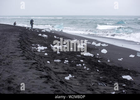 DIAMOND BEACH, JOKULSARLON, ISLAND - 22. MAI 2019: Touristen bewundern und Fotografieren der schmelzenden Eisbergen auf dem Atlantik Küste in Jokulsarlo Stockfoto