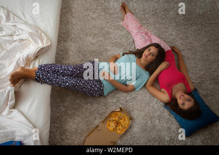 Blick von oben auf die beiden jungen Mädchen auf dem Boden liegend in Ihrem Haus mit Pizza an Ihrer Seite Stockfoto