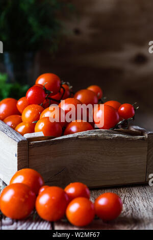 Kiste frisch gepflückte Bio Kirschtomaten auf rustikalen Holztisch, auf Basis pflanzlicher Lebensmittel, Nahaufnahme, selektiver Fokus Stockfoto