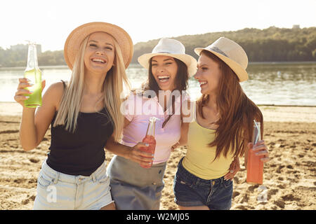 Gruppe Junger stilvolle glückliche Frauen treffen am Strand Cocktails mit und Lachen im Sonnenlicht Stockfoto