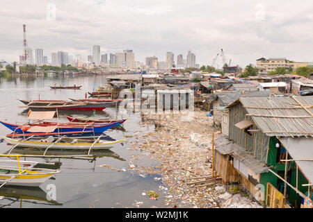 Die Slums von Manila auf dem Hintergrund einer großen Stadt. Häuser und Boote der armen Bewohner von Manila. Wohnung die Armen in den Philippinen. Stockfoto