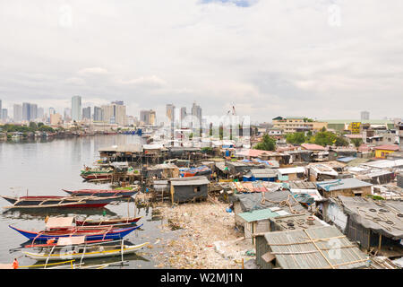 Die Slums von Manila auf dem Hintergrund einer großen Stadt. Häuser und Boote der armen Bewohner von Manila. Wohnung die Armen in den Philippinen. Kontrast sozialen Schichten. Stockfoto