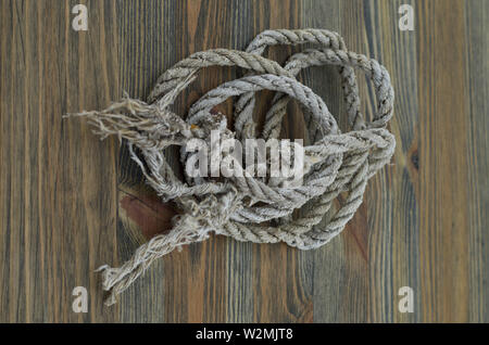 Vintage Seil, alte Seil ruht auf Holzbrett. Mit Knoten an den Enden eingerollt. Ready-to-use Seil. Stockfoto