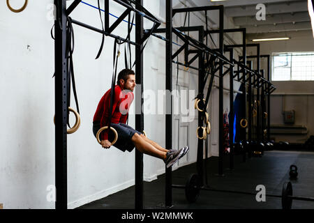 Seitenansicht des männlichen Athleten Training in der Turnhalle mit Gymnastik Ringe Stockfoto