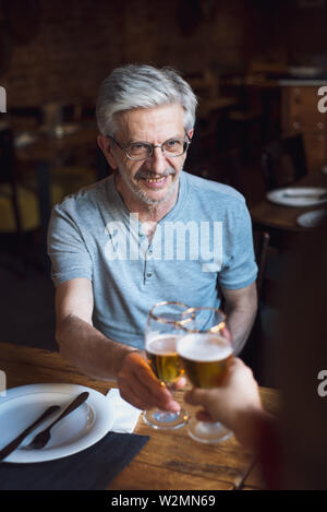 Älterer Mann toasten, mit einem Bier in der Bar Stockfoto