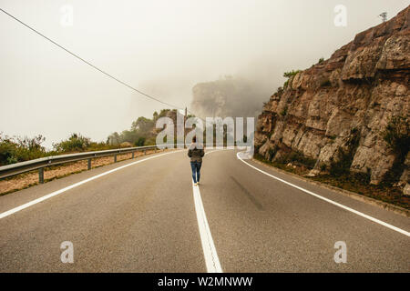 Person zu Fuß entlang der Mittellinie in einem Straße schlängelt sich durch die Berge des Monestir De Montserrat Region in der Nähe Barcelona Spanien auf einem nebligen Tag Stockfoto