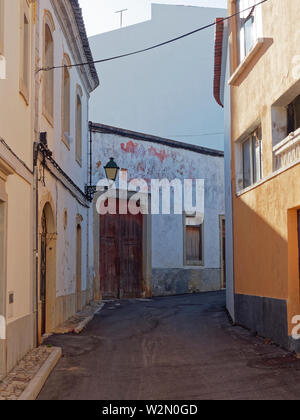 Eine schmale Straße während der Siesta in der kleinen portugiesischen Stadt Estoi an der Algarve, mit einem reich verzierten Straßenlaterne an der Wand des Hauses befestigt Stockfoto