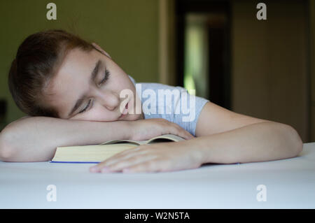 Gefoltert Mädchen liest ein Buch auf dem Tisch und sie ist sehr müde und möchte schlafen, gähnt, schläft beim lesen Geschichten und lehren Stockfoto