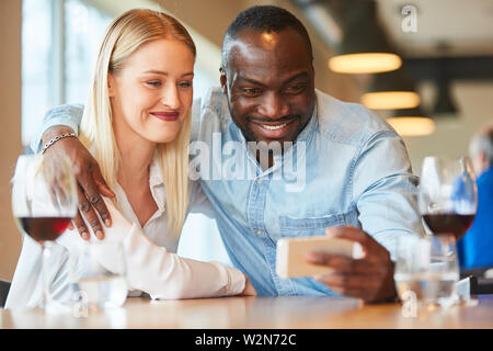 Multikulturelle Paare ein selfie mit Smartphone während dating Im Restaurant Stockfoto