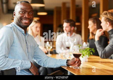 Junge afrikanische Mann mit einem Glas Wein und Freunden im Restaurant Stockfoto