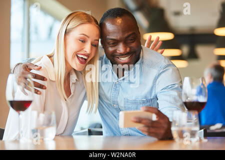 Lachende junge Frau und afrikanischen Freund eine selfie im Restaurant nehmen Stockfoto