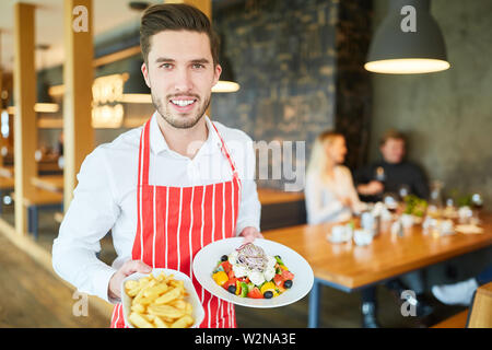 Junger Mann als eine freundliche Kellner im Restaurant serviert Vorspeisen Stockfoto