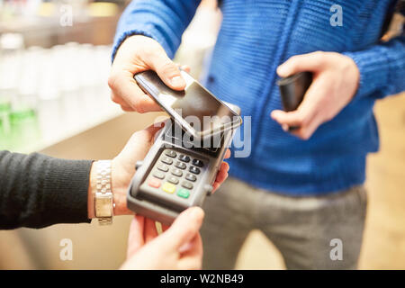 Kunde zahlt berührungslos mit Smartphone über NFC an der Card Terminal in einem Restaurant Stockfoto