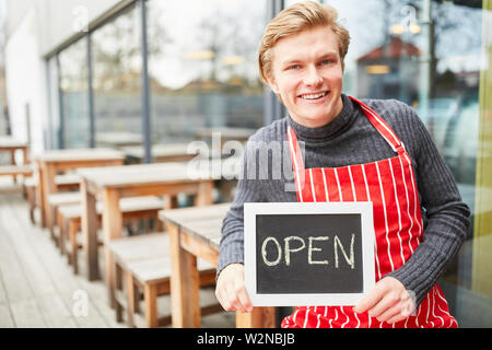 Junger Mann als Kellner oder Gründer mit kreidetafel vor einem Café oder Bistro Stockfoto