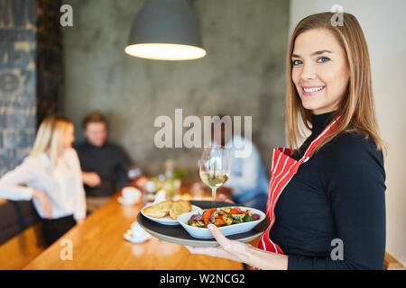 Junge Frau als freundliche Kellnerin serviert Vorspeisen im Restaurant Stockfoto
