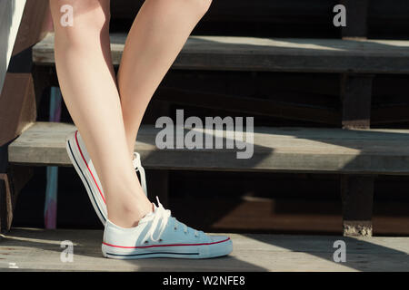 Mädchen in Turnschuhen stehend auf die Schritte, die bei sonnigem Wetter. Bequeme Schuhe für die Stadt. Stockfoto