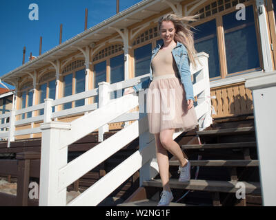 Junge fröhliches Mädchen, der am Ufer des Meeres. Junge blonde Frau lächelnd. Junge trendige Frau auf einem Spaziergang, Lifestyle. Stockfoto