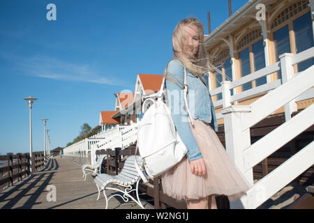 Junge fröhliches Mädchen, der am Ufer des Meeres. Junge blonde Frau lächelnd. Junge trendige Frau auf einem Spaziergang, Lifestyle. Stockfoto