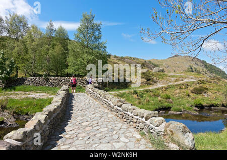 Wanderer Menschen zu Fuß über Steinbrücke und Wanderweg Watendlath im Sommer Lake District National Park Cumbria England Großbritannien Großbritannien Stockfoto