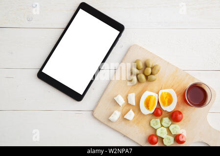 Tablet, Tee und türkischen, mediterranen Frühstück vor dem Beginn des Arbeitstages oder während der Arbeit auf einem hellen Holz- Fach auf einem weissen natürlichen backgrou Stockfoto