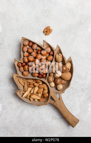 Andere Art von Muttern in Holz Tablett auf konkreten Hintergrund. Haselnuss, Mandel, Pecan, Nussbaum in Holz- Teller auf Beton. Vertikale Flach, Ansicht von oben, c Stockfoto