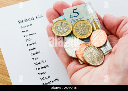 Eines armen älteren Rentner Hand eine kleine Menge neues Geld GBP mit einer Einkaufsliste für Lebensmittel Armut strenge Konzept England Großbritannien Großbritannien Stockfoto