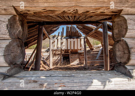 Blick durch ein Fenster in einen alten hölzernen Jurte. Rahmen aus dem Fenster. Melden Sie sich an der Wand, Barren. Innerhalb der Säulen und Gras. Stockfoto