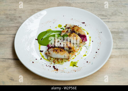 Nahaufnahme der gefüllte Calamari squid, mit Cous Cous, Oliven, Gemüse, Zucchini pürieren, Sahne, Basilikum und frischen Kräutern, Olivenöl, gesunde foo serviert. Stockfoto