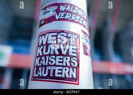 Kaiserslautern, Deutschland. 10. Juli 2019. Fußball, 3.Liga: 1.FC Kaiserslautern Foto Session für die Saison 2019/20 im Fritz-Walter-Stadion. Aufkleber mit der Aufschrift 'Waldhof verrecke" - eine Anspielung auf den Waldhof Mannheim Verein - und "Westkurve Kaiserslautern' sind zu einem Fahnenmast an einem Stadion Eingang angeschlossen ist. Foto: Uwe Anspach/dpa/Alamy leben Nachrichten Stockfoto