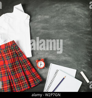 Notebook Schuluniform für ein Mädchen shirt Rock ein Wecker Kreidetafel. Das Konzept der zurück zu Schule und Bildung. Stockfoto