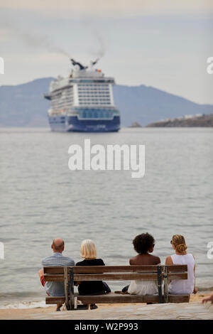 Mykonos, griechische Insel Mikonos, Teil der Kykladen, Griechenland. Touristen auf a waterfront Beach Bank auf Berühmtheit Kante zuerst Edge-Klasse Kreuzfahrt s Stockfoto