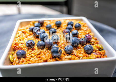 Makro Nahaufnahme des Goldenen gebackenes Müsli Müsli Schale aus Hafer Haferflocken und Samen Nüsse mit frischen Blaubeeren in moderne quadratische Teller Teller Schüssel gemacht Stockfoto