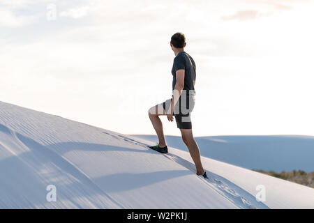 Man Klettern Gehen auf Sand Hill in White Sands Dunes National Monument in New Mexico bei Sonnenuntergang auf der Suche Stockfoto