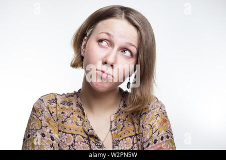 Ein portrait Foto eines flirtatious, kokett junge Mädchen mit mittleren blonde Haare. Schmollen und Suchen kokett, flirty auf Grau studio Hintergrund. beleidigt Frau. skittish, schmollen, schmollen Teenager Stockfoto