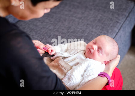 Ein winziges Neugeborenes baby boy liegen auf einem womans' schoss ihr Finger halten. Das Baby ist friedlich eingeschlafen ist in einer Strickjacke gewickelt Stockfoto