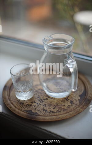 Krug Wasser und ein Glas in einem Fach auf der Fensterbank Stockfoto