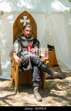 Nis, Serbien - Juni 15. 2019 Ritter in Trachten sitzt auf einem hölzernen Thron vor dem Zelt und Getränke Wein auf Ritter Festival Stockfoto